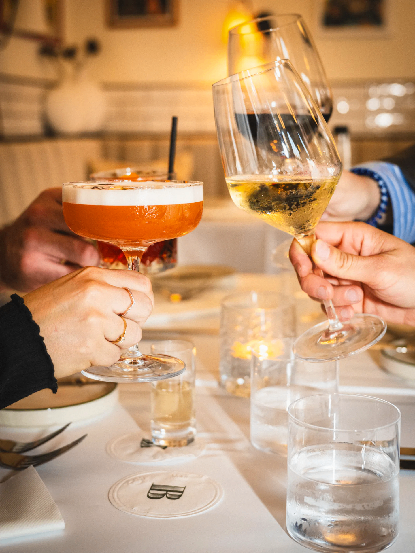 Cocktail and wine glasses raised in a toast at a Bastion-monogrammed table